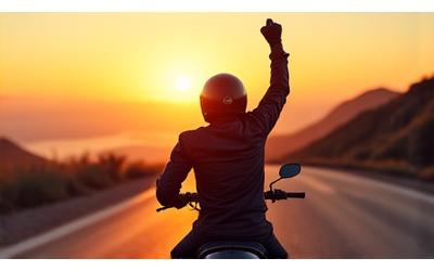 Rider in RoadWarrior Gear helmet on a winding road, arm raised in triumph.